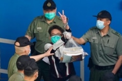 Pro-democracy activist Figo Chan shows a victory sign as he is escorted by Correctional Services officers to a prison van for a court in Hong Kong, May 28, 2021.
