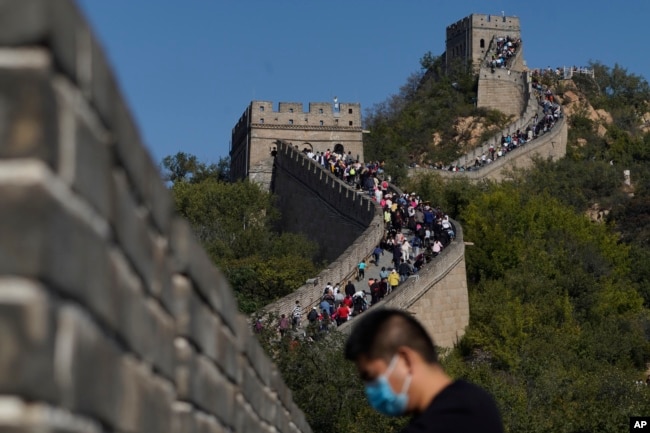 FILE - A man wearing a mask to help protect from the coronavirus stands near a stretch of the Badaling Great Wall of China on the outskirts of Beijing on Oct. 6, 2020. Authorities in China arrested the two men for smashing a path through a section of the ancient wall, a cultural icon and United Nations heritage site. (AP Photo/Ng Han Guan, File)