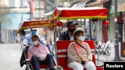 Foreign tourists wear protective masks while traveling on three-wheel cycle along old quarters streets in Hanoi, Vietnam March 17, 2020. REUTERS/Kham