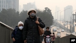 A woman and a child wearing masks walk hands in hands as a cyclist covers his nose for protection against the pollution on a pedestrian overhead bridge on a polluted day in Beijing, Sunday, Dec. 20, 2015.