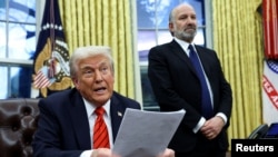 Presidente dos Estados Unidos, Donald Trump, lê sobre as taxas sobre o aço e o alumínio, com Howard Lutnick em segundo plano, no Salão Oval da Casa Branca, em Washington, 10 de fevereiro de 2025