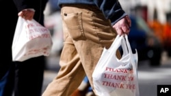 FILE - Pedestrians carry plastic bags in Philadelphia, March 3, 2021. Giving out single-use plastic bags in the city became illegal this fall, but penalties don’t start until April 1.