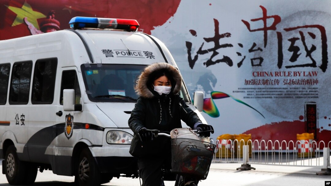 A woman and a police van pass a Chinese government propaganda billboard that reads "China Rule By Law" on a street in Beijing, Dec. 28, 2016. Many in China are infuriated by a decision to drop charges in a high-profile police brutality case.