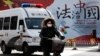 A woman and a police van pass a Chinese government propaganda billboard that reads "China Rule By Law" on a street in Beijing, Dec. 28, 2016. Infuriated by a decision by Beijing prosecutors to drop charges in a high-profile police brutality case, universi