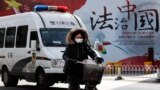 A woman and a police van pass a Chinese government propaganda billboard that reads "China Rule By Law" on a street in Beijing, Dec. 28, 2016. Infuriated by a decision by Beijing prosecutors to drop charges in a high-profile police brutality case, universi