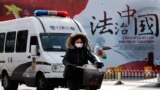 A woman and a police van pass a Chinese government propaganda billboard that reads "China Rule By Law" on a street in Beijing, Dec. 28, 2016. Infuriated by a decision by Beijing prosecutors to drop charges in a high-profile police brutality case, universi