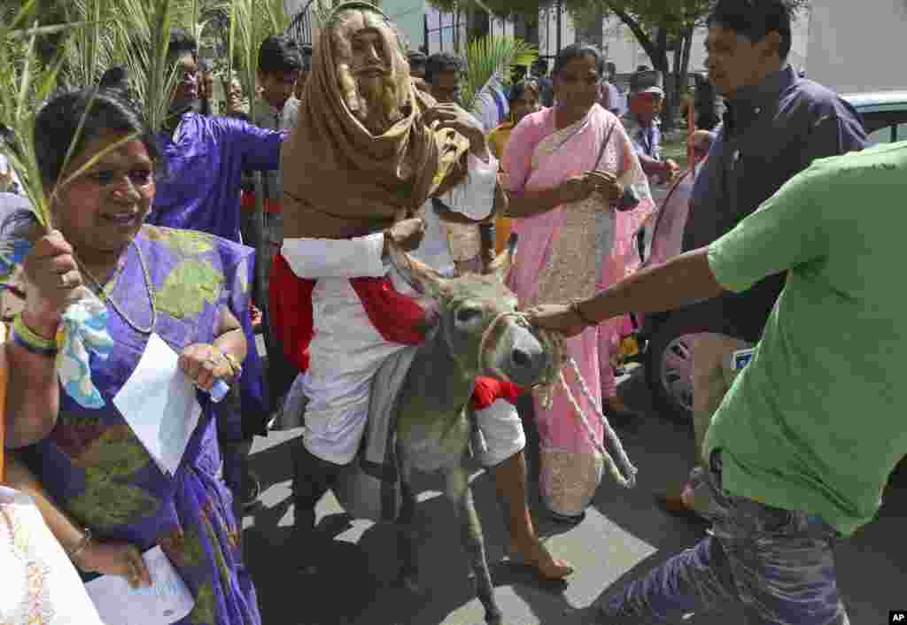An Indian Christian devotee dressed like Jesus Christ sits on a donkey as others hold palm leaves during a Palm Sunday procession in Hyderabad, India.