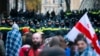 Protesters with a Georgian national flag stand in front of police blocking the entrance of the Parliament's building during a rally to demand new parliamentary elections in the country, in Tbilisi, Georgia, Nov. 25, 2024. 