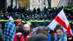 Protesters with a Georgian national flag stand in front of police blocking the entrance of the Parliament's building during a rally to demand new parliamentary elections in the country, in Tbilisi, Georgia, Nov. 25, 2024. 