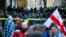 Protesters with a Georgian national flag stand in front of police blocking the entrance of the Parliament's building during a rally to demand new parliamentary elections in the country, in Tbilisi, Georgia, Nov. 25, 2024.