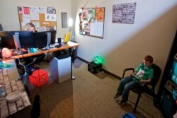 FILE - Katie Arnold works at her office while her son Rowen, 7, plays educational games on her iPad in Portland, Ore. Rowen has been spending his days in his mother's office, where she manages accounts for a catering company.