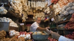 A vendor exchanges money with a customer at a shop selling garlic, onions and potatoes at a wholesale market in Mumbai. India's food price index rose 8.76 percent in the year to April 16, government data showed.
