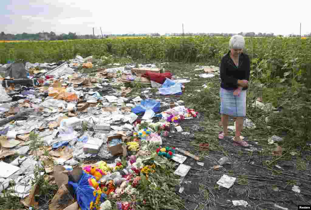A local resident stands near flowers and mementos placed at the crash site of Malaysia Airlines Flight MH17, near the settlement of Rozspyne in the Donetsk region, July 19, 2014.