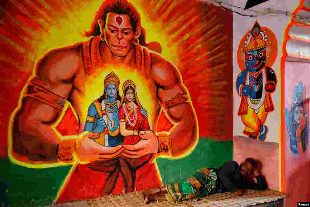 A man lies on a bed, beside a wall painted with Hindu religious figures in Dhaka, Bangladesh.