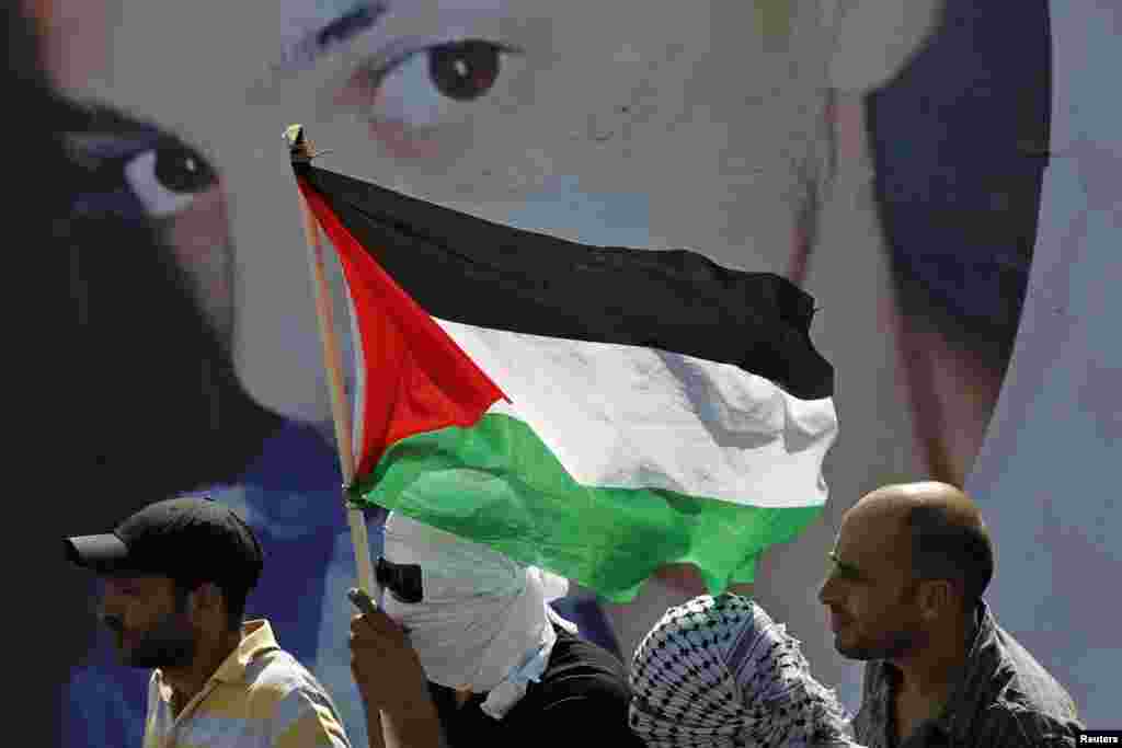 Palestinians look on as they stand in front of a poster depicting 16-year-old Mohammed Abu Khudair during his funeral in Shuafat, an Arab suburb of Jerusalem, July 4, 2014.