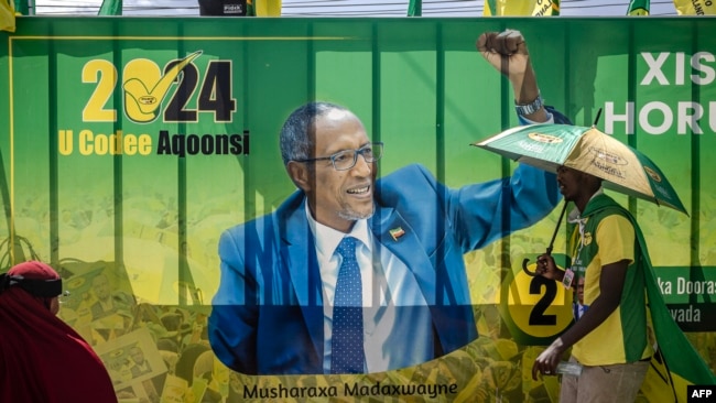 A supporter of the ruling Kulmiye party walks past a banner showcasing the incumbent president of Somaliland and presidential candidate Muse Bihi Abdi following Kulmiye's final campaign rally in Hargeisa on Nov. 9, 2024.