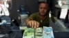 A currency exchange shop employee shows 100 Euros, 100 U.S. dollars and 100 Turkish Liras banknotes at his shop at a market street in Istanbul, Thursday, July 30, 2020. The Turkish Lira continued its trend down against the U.S. dollar Thursday but…