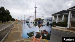 Photographer Carlos Barria holds a print of a photograph he took in 2005, as he matches it up at the same location 10 years on, in New Orleans, United States, August 16, 2015. The print shows Errol Morning sitting on his boat on a flooded street…