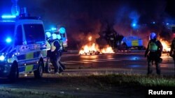 Petugas polisi berjalan di dekat ban dan palet yang terbakar selama kerusuhan di lingkungan Rosengard di Malmo, Swedia, sebagai ilustrasi (Foto: Reuters)