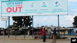 Deux hommes se tiennent sous une affiche géante montrant des conseils sur la façon de prévenir la propagation du coronavirus, à Harare, Zimbabwe, le 5 avril 2020.