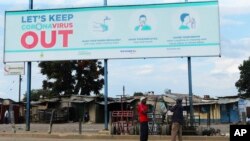 FILE - Two men stand underneath a giant poster showing advice on how to prevent the spread of the coronavirus, in Harare, Zimbabwe, April, 5, 2020. 