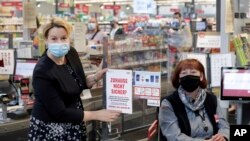 German Minister for Family Affairs, Franziska Giffey, left, attaches a sticker at the register of cashier Kerstin Strasen, right, in a supermarket in Berlin, as part of a nationwide cooperation of supermarkets against domestic viloence, April 29, 2020.