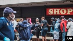 A South African policeman points his weapon to disperse shoppers outside a supermarket in Johannesburg, on March 28, 2020, while trying to enforce a safe distance amid concern of the spread of COVID-19.