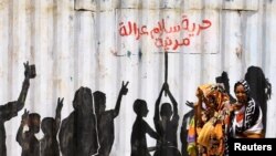 Warga berjalan melintasi grafiti dalam bahasa Arab yang artinya "Kemerdekaan, Perdamaian, Keadilan, dan Masyarakat Sipil," di distrik Burri, Khartoum, Khartoum, Sudan, 10 Juli 2019. 