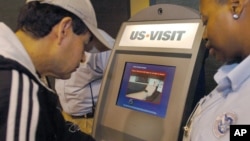 FILE - Department of Homeland Security official (r) assist a passenger (l) as he scans his fingerprint on a machine, part of the exit process at Hartsfield-Jackson Atlanta International Airport in Atlanta. The White House said the country's homeland security agency is immediately altering its electronic visa-free clearance system.