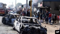 FILE: Pedestrians pass burnt out cars on the side of a street on the outskirts of Johannesburg, Monday Sept. 2, 2019.