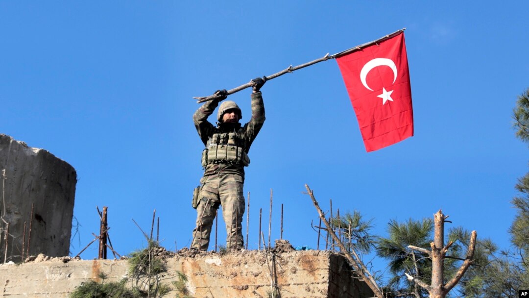 Seorang tentara mengibarkan bendera Turki setelah militer Turki berhasil menguasai bukit Bursayah, yang memisahkan kota Afrin, Suriah yang dikuasai milisi Kurdi, dengan kota Azaz yang dikuasai Turki (28/1). 