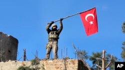 Seorang tentara mengibarkan bendera Turki setelah militer Turki berhasil menguasai bukit Bursayah, yang memisahkan kota Afrin, Suriah yang dikuasai milisi Kurdi, dengan kota Azaz yang dikuasai Turki (28/1). 