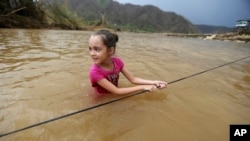 Ruby Rodriguez, 8, looks back at her mother as she wades across the San Lorenzo Morovis river with her family, since the bridge was swept away by Hurricane Maria, in Morovis, Puerto Rico, Sept. 27, 2017. They were returning to their home after visiting family.