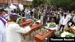 ARCHIVO - Un sacerdote con una máscara facial por la pandemia de coronavirus rocía agua bendita sobre los ataúdes durante el funeral de cinco menores que fueron asesinados en la ciudad de Cali, Colombia, 14 de agosto 2020.