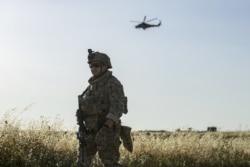 FILE - A U.S. soldier stands guard as a Russian military helicopter flies over the northeastern Syrian town of Malikiyah at the border with Turkey, June 3, 2020.