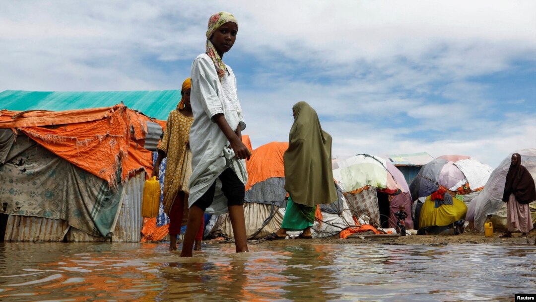 Warga menyeberangi air banjir di tempat penampungan sementara mereka di kamp Al-Hidaya untuk para pengungsi setelah hujan lebat di pinggiran Mogadishu, Somalia, 19 November 2023. (Foto: Reuters)