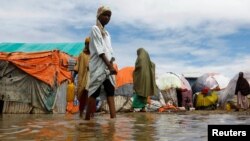 Warga menyeberangi air banjir di tempat penampungan sementara mereka di kamp Al-Hidaya untuk para pengungsi setelah hujan lebat di pinggiran Mogadishu, Somalia, 19 November 2023. (Foto: Reuters)