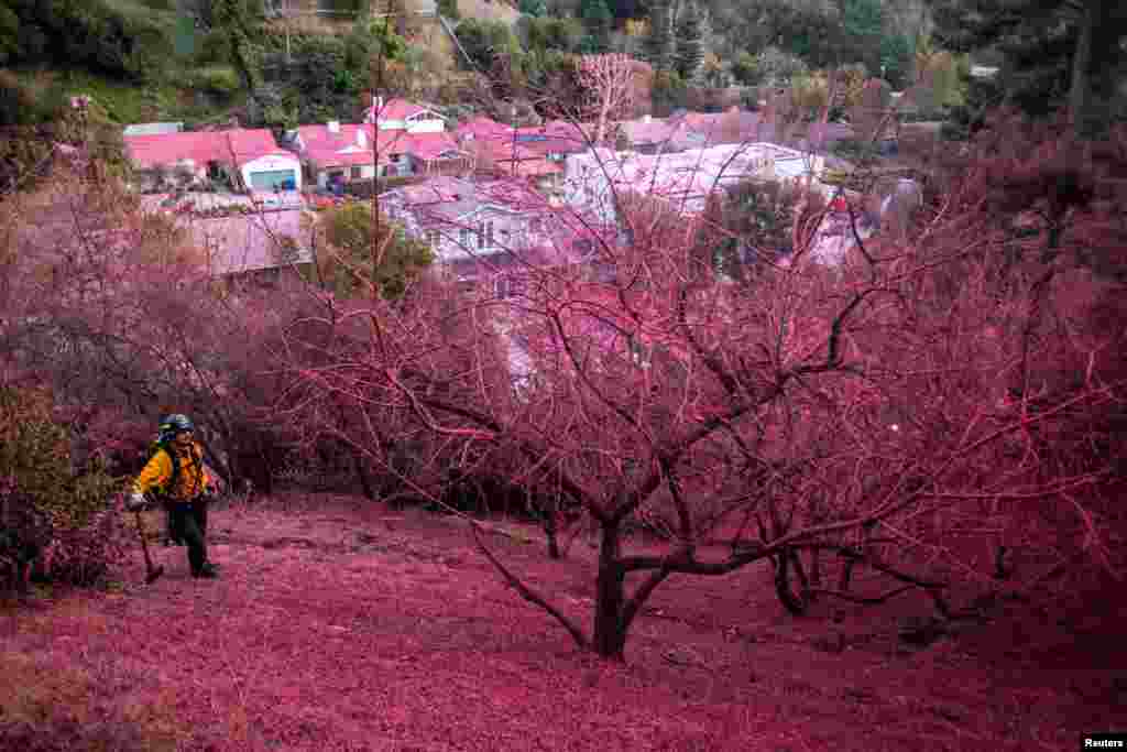 A firefighter stands on a hillside covered with retardant as the Palisades Fire, one of several simultaneous blazes that have ripped across Los Angeles County, burns in Mandeville Canyon, a neighborhood of Los Angeles, California, Jan. 12, 2025. 