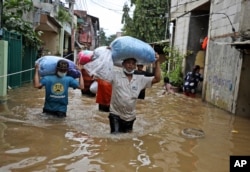 FILE - Indonesian men carry their belongings as they wade through the water at a flooded neighborhood following heavy rains in Jakarta, Indonesia, Friday, Feb. 19, 2021. (AP Photo/Dita Alangkara)