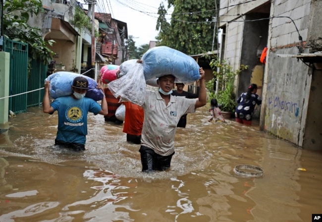 FILE - Indonesian men carry their belongings as they wade through the water at a flooded neighborhood following heavy rains in Jakarta, Indonesia, Friday, Feb. 19, 2021. (AP Photo/Dita Alangkara)