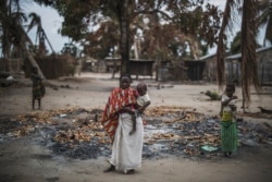A woman holds her child while standing in a burned out area in the attacked village of Aldeia da Paz outside Macomia in Cabo Delgado Province, in Mozambique, on Aug. 24, 2019.