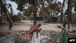 FILE - A woman holds her child while standing in a burned out area in the attacked village of Aldeia da Paz outside Macomia in Cabo Delgado Province, in Mozambique, Aug. 24, 2019.