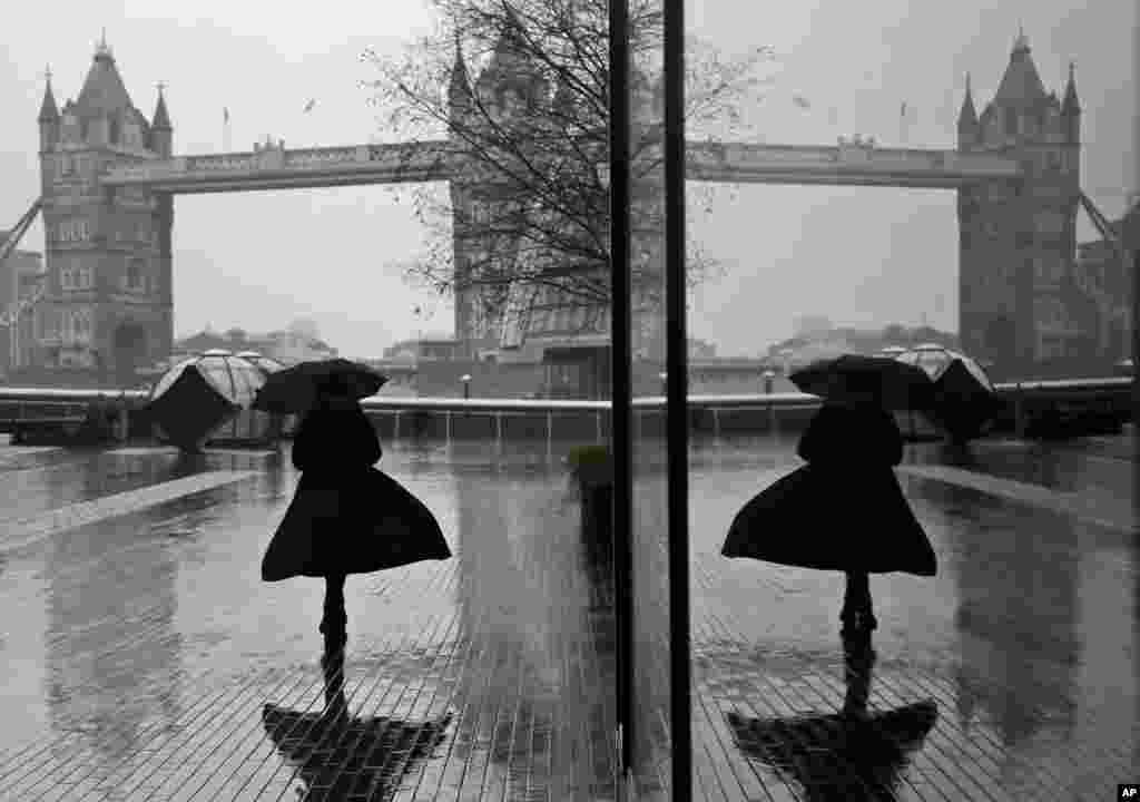 A woman is reflected in a window as she walks through wind and rain toward Tower Bridge in London during England&#39;s third national lockdown to curb the spread of coronavirus.