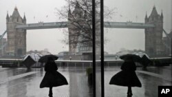 A woman is reflected in a window as she walks through wind and rain toward Tower Bridge in London during England's third national lockdown to curb the spread of coronavirus.