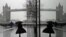 A woman is reflected in a window as she walks through wind and rain toward Tower Bridge in London during England's third national lockdown to curb the spread of coronavirus.