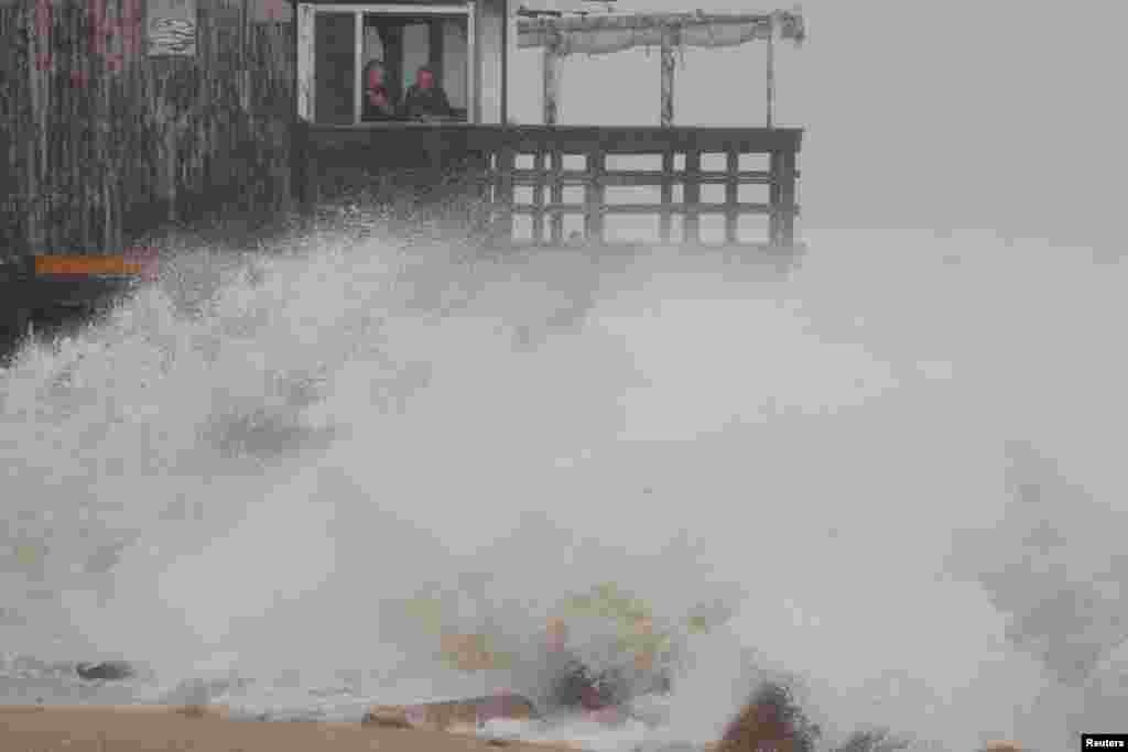 People watch as the waves crash around the Ocean Mist bar as Tropical Storm Henri approaches South Kingstown, Rhode Island.