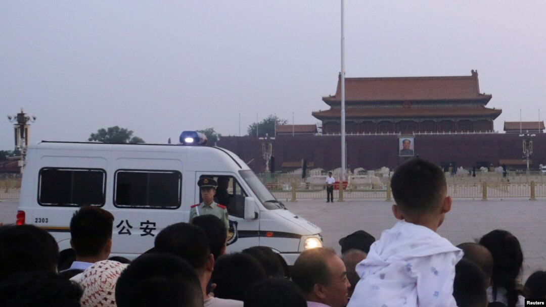 Seorang polisi paramiliter berjaga di depan sebuah mobil polisi saat para pengunjung menunggu upacara penaikan bendera di Alun-alun Tiananmen saat matahari terbit di Beijing, China, 4 Juni 2019.
