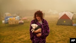 Shayanne Summers holds her dog Toph while wrapped in a blanket after several days of staying in a tent at an evacuation center at the Milwaukie-Portland Elks Lodge, Sept. 13, 2020, in Oak Grove, Oregon.