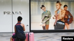 FILE - A man sits on suitcases in front of an advertising window of luxury goods retailer Prada in Tokyo, August 25, 2015. (REUTERS/Thomas Peter)