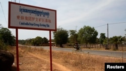 A man rides a motorcycle past a signboard for the Cambodia Iron Group at the Rovieng District in Preah Vihear province, February 10, 2013.